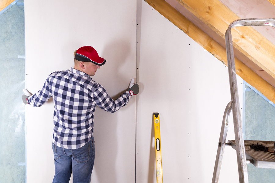 Construction worker holding gypsum board. Attic renovation. Installation of drywall